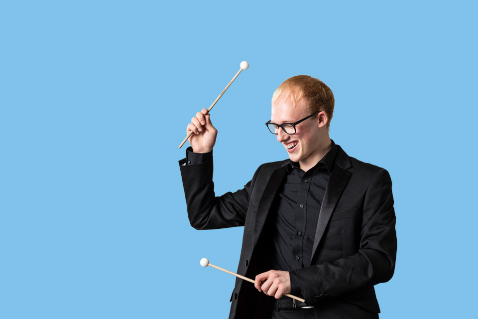 Smiling male percussion student on a pale blue background
